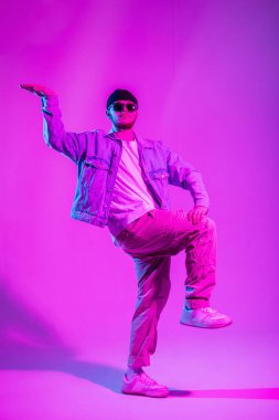 Yakışıklı, başarılı hippi dansçı şapkalı ve güneş gözlüklü şık kotlu yaratıcı pembe ve neon ışıklı dansçı.