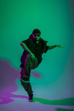 Siyah gözlüklü, havalı profesyonel dansçı yaratıcı renkli stüdyoda yeşil ve pembe ışıklı dans ediyor.