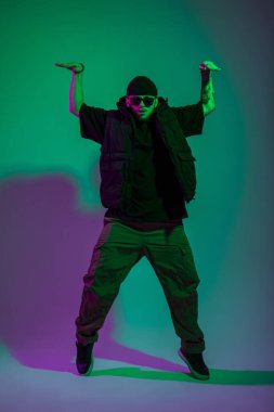 Profesyonel dansçı, güneş gözlüklü, moda elbiseli yaratıcı stüdyoda pembe ve yeşil renkte dans ediyor.