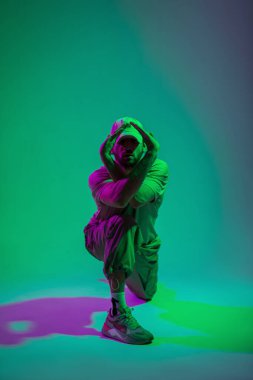 Şapkalı ve spor ayakkabılı yakışıklı profesyonel dansçı. Renkli stüdyoda dans ediyor. Cyan ve pembe ışıklarla.
