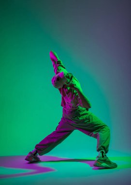 Havalı, modaya uygun, moda kıyafetleri içinde, yeşil ve mor ışık saçan yaratıcı bir stüdyoda dans eden şık bir erkek dansçı.