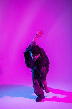 Havalı trend adam profesyonel dansçı siyah moda kıyafetleri içinde stüdyoda pembe ve neon ışıkta dans ediyor.