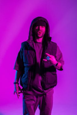 Moda kıyafetleri içinde havalı genç dansçı kapüşonlu pozlar ve yaratıcı renk stüdyosunda pembe ve neon ışıklı ifade.