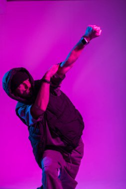 Yakışıklı, şık, genç, profesyonel dansçı, modaya uygun, siyah elbiseli, yelekli adam pembe ve mavi ışıklı yaratıcı bir stüdyoda dans ediyor.