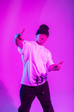Beyaz tişörtlü şık erkek dansçı pembe ve neon ışıklı yaratıcı stüdyoda kameraya bakıyor.