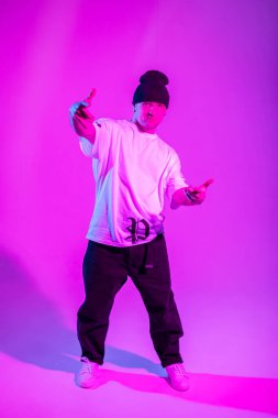 Modaya uygun profesyonel break dans dansçısı şık kıyafetler içinde yaratıcı bir stüdyoda pembe ve neon ışıklarla dans ediyor.