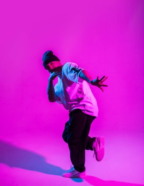 Moda kıyafetleri içinde yakışıklı break dansçı yaratıcı stüdyoda pembe ve neon ışıklı dans ediyor.