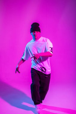 Havalı break dansçı şık kıyafetli adam pembe arka planda dans ediyor neon ışıklarıyla.
