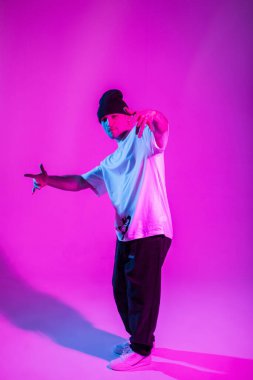 Pembe ve neon ışıklı yaratıcı bir stüdyoda şapkalı havalı dansçı çocuk poz veriyor ve dans ediyor.
