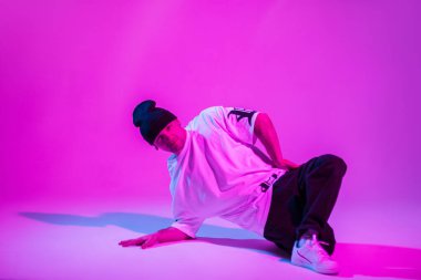 Moda kıyafetli profesyonel break dansçı yaratıcı stüdyoda pembe ve neon ışıklı dans ediyor.