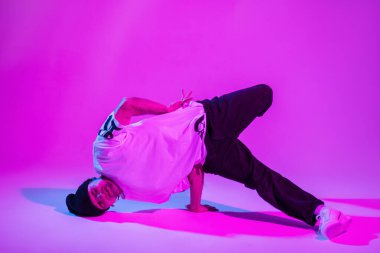 Modaya uygun hippi hippi dansçı şapkalı, tişörtlü, kot pantolonlu ve spor ayakkabılı neon ışıklı yaratıcı pembe bir stüdyoda dans ediyor..