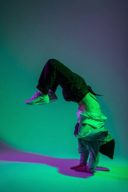 Yakışıklı hip hop dansçısı B-boy modaya uygun kotlar içinde dans ediyor ve ellerinde yeşil ve mor ışıkla yaratıcı bir renk stüdyosunda duruyor.