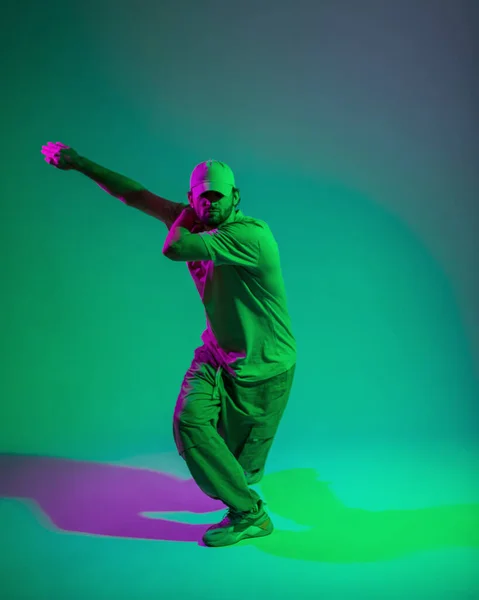 stock image Stylish fashion dancer professional man with a cap in trendy outfit with sneakers dances in motion in a creative studio with green and pink light
