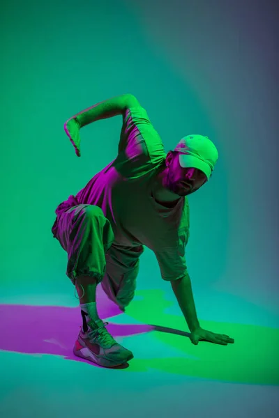 stock image Cool trendy professional hip hop dancer man with cap in fashion clothes dancing in a colorful studio with green and pink lights