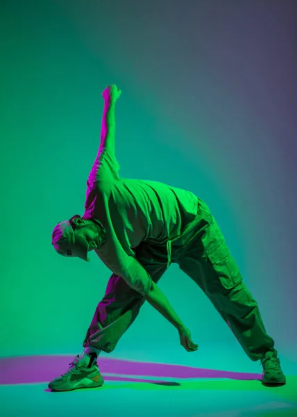 stock image Cool trendy stylish male professional dancer in trendy clothes with a cap and sneakers is dancing in a creative studio with magenta and cyan light