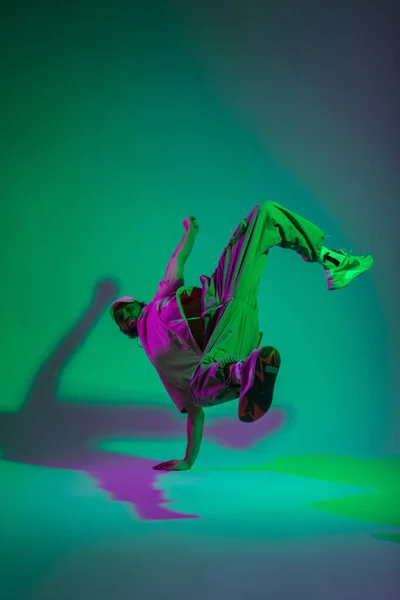Fashionable professional hip hop dancer man b-boy in fashion trendy clothes with a cap and stylish sneakers dances on his hands in a creative color studio with cyan and magenta light