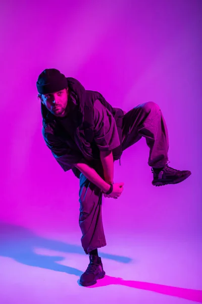 stock image Fashion handsome professional dancer man with hat in stylish trendy clothes with vest and sneakers dance in motion in creative color studio with pink and neon lights