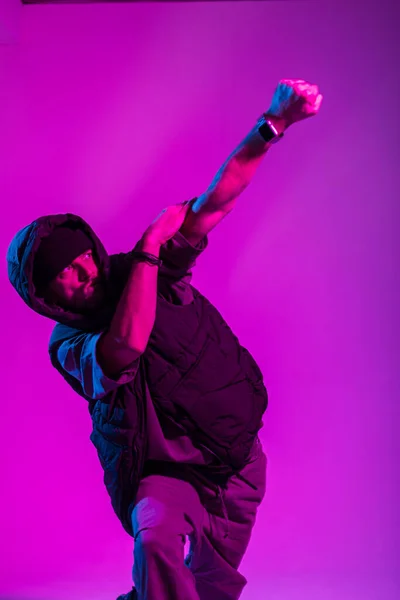 stock image Handsome stylish young professional dancer guy man in trendy fashion black clothes with a vest dances in motion in a creative studio with pink and blue light