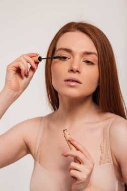 Güzel, genç, kızıl saçlı, temiz tenli bir bayan model stüdyoda makyaj ve rimel kirpikleri yapıyor. Güzellik