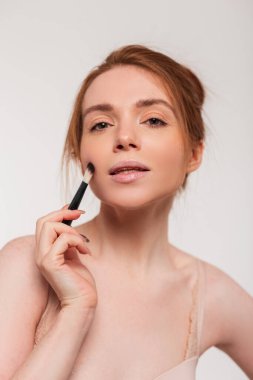 Makyaj fırçası tutan temiz ciltli, kızıl saçlı güzel bir kız. Güzellik ve kozmetik