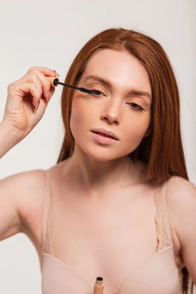 stock image Fresh beautiful redheaded Scandinavian lady model paints her lashes with mascara on a white background. Beauty and makeup