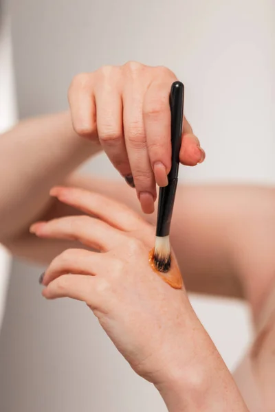 Beautiful young woman holds a makeup brush and applies highlighter cream on her hand, close-up, Beauty and makeup