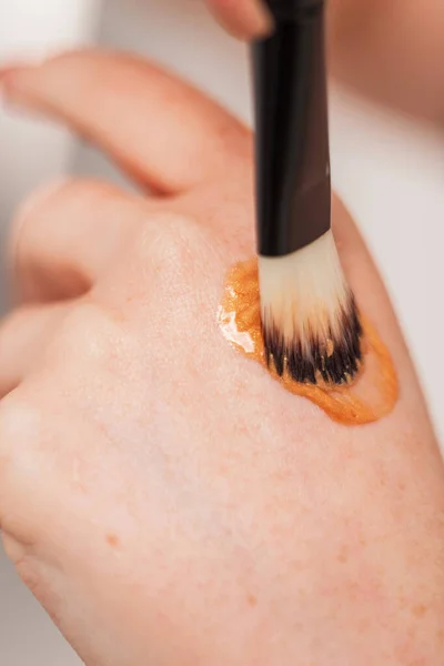 Girl doing makeup with highlighter cream on her hand and a brush, closeup. Beauty and skin care