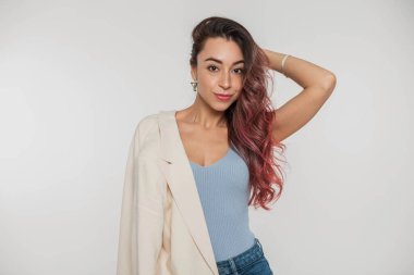 Çilli, pembe saçlı, mavi bluzlu, kot pantolonlu, omzunda beyaz bir arka planda ceketi olan güzel bir kadın.