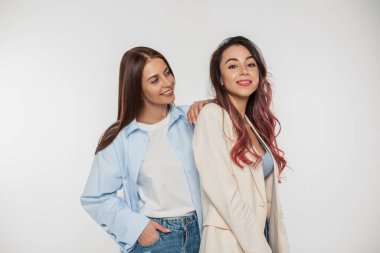 Moda kıyafetleri içinde genç, güzel, mutlu moda kızlar stüdyoda beyaz bir arka planda duruyorlar.