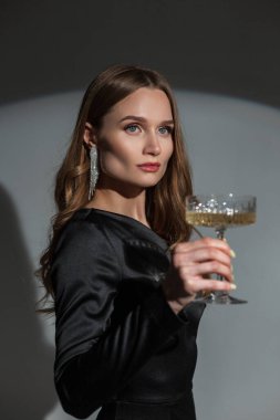 Stüdyo bayan portresi. Güzel stil sahibi bir kadın. Elmas küpeli, modaya uygun siyah zarif bir elbise ve bir partide bir bardak şampanya. Güzel bayan bir olayı kutluyor.