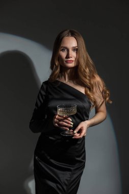 Moda siyah elbisesi içinde pırlanta küpeli şık, zarif bir kadın. Siyah arka planda bir bardak şampanya ve bir partide dairesel bir ışık. Kız doğum gününü bile kutluyor.