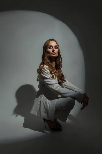 stock image Fashionable beautiful stylish woman model in fashion white suit with blazer sitting and posing in studio on dark background