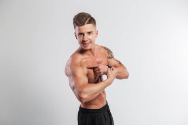 Yakışıklı, mutlu, kaslı, kaslı, güzel, çıplak, şişmiş gövdeli bir adam, stüdyoda beyaz bir arka planda, pazıların ve noktaların kaslarını gösteriyor. Antrenman zamanı.