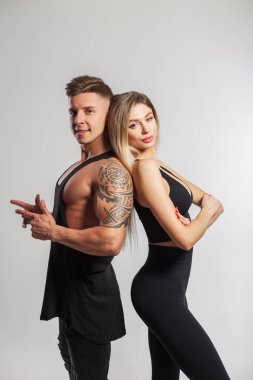 Stüdyoda arka arkaya poz veren güzel genç atletik çift. İnce vücutlu güzel genç fitness kızı ve siyah spor giyimli yakışıklı kaslı atletik adam.