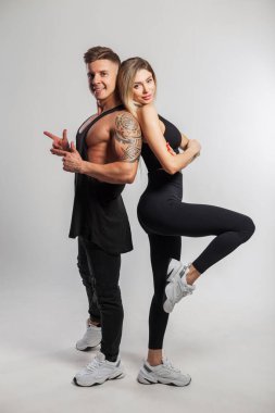Beyaz arka planda şık spor kıyafetleri içinde güzel mutlu bir çift. Yakışıklı kaslı adam ve güzel fitness kadını stüdyoda durup poz veriyor.