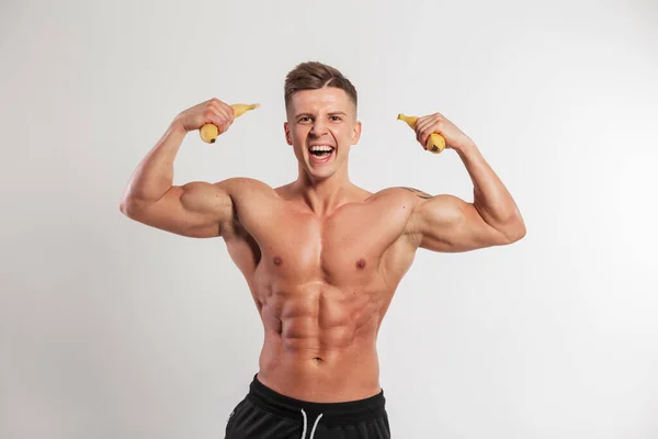 一个肌肉发达的有趣的运动肌肉男拿着香蕉 在白色的背景上表现出二头肌 健康的纯素食饮食和运动 — 图库照片