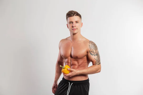 Handsome sport fitness trainer vegan man with muscular body holding yellow pepper on white background in studio