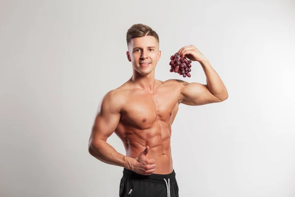 身强体壮的英俊男子拿着葡萄 在演播室里有着白色背景 健康的生食和体育运动 — 图库照片