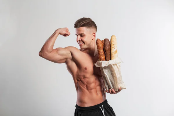健康な筋肉質ボディの男に合うハンサムな幸せな筋肉運動選手は紙袋のパンのバゲットを保持し 白い背景の二足を示す 健康食品とベーキング — ストック写真