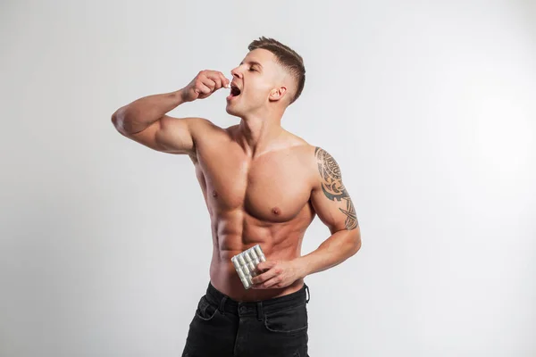 Handsome strong athletic fit guy with a muscular body holds vitamins and drinks pills on a white background in the studio. Sports nutrition and supplements, concept