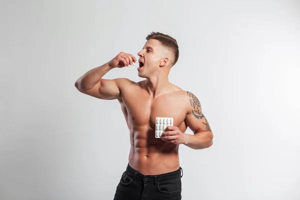 セクシーな体を持つ運動能力の強い筋肉ハンサムな男は 白い背景に丸薬と飲み薬のパックを保持しています スポーツ — ストック写真