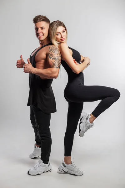 stock image Beautiful happy sports couple posing in the studio on a white background. Beautiful slim fitness girl and muscular handsome man in black sportswear with sneakers