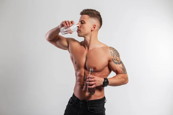 筋肉質の体を持つハンサムな筋肉適性の人は白い背景のガラスから水及び飲料水のボトルを保持する 健康と水のバランス — ストック写真