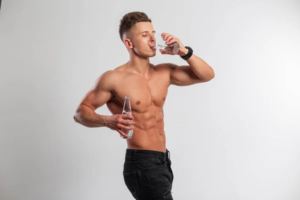 英俊的肌肉发达的男子赤身裸体 拿着一瓶水 喝着白色背景的杯子里的水 水平衡与健康 — 图库照片
