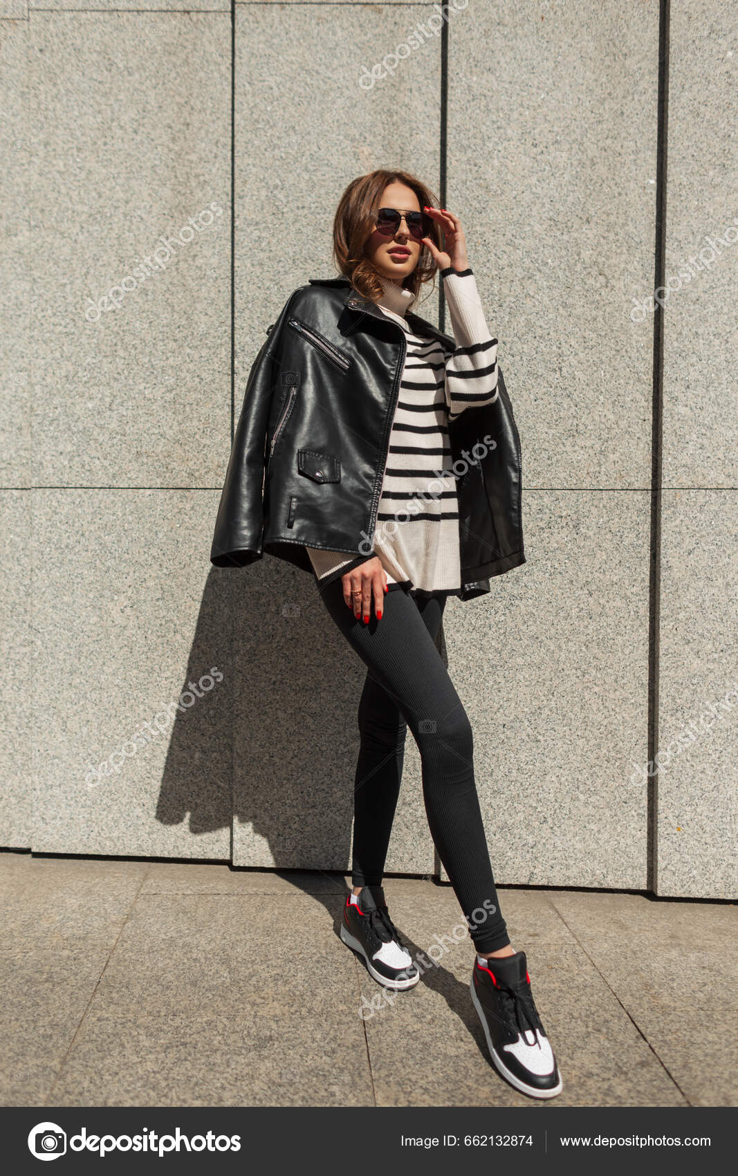 Moda jovem e bonita mulher com óculos de sol em roupa casual de rua com  jeans de jaqueta de couro e sapatos brancos caminha perto do shopping de  construção de tijolos vintage