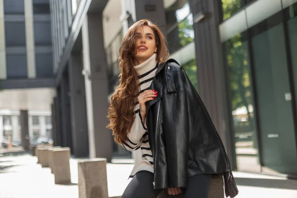 Premium Photo  Beautiful young fashionable woman in urban fashion outfit  with a long leather coat black top and high waisted jeans with a purse is  walking outside the building