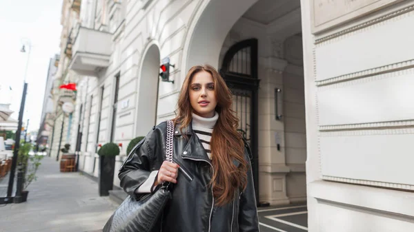 在欧洲城市里 穿着时尚服装 穿着皮革黑色夹克 头戴时髦手提包的漂亮辣妹在散步 — 图库照片
