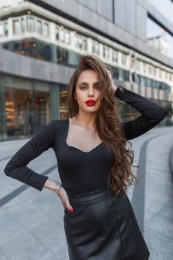Şık, güzel, seksi, zarif, kırmızı dudaklı, modaya uygun siyah elbiseli bir kadın şehirde yürüyor.