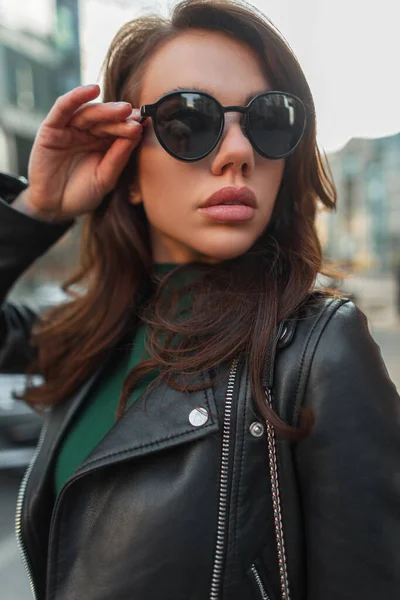 漂亮漂亮的年轻女士穿着时髦的衣服 穿着皮夹克 戴着时髦的太阳镜 走在城市里 — 图库照片