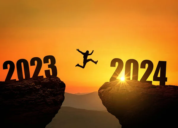 Man jumping on cliff 2024 over the precipice at amazing sunset. New Year\'s concept. Symbol of starting and welcome happy new year 2024. People enters the year 2024, creative idea